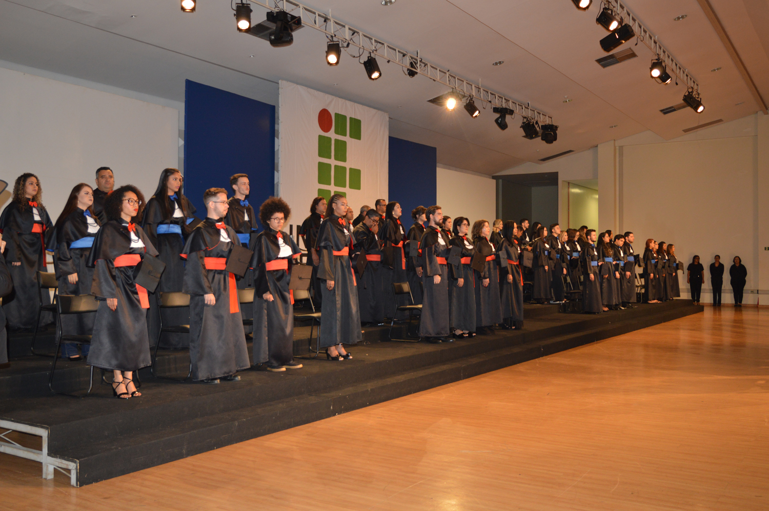 Imagem dos formandos posicionados no tablado montado no palco do Centro de Eventos da UFG, momentos antes do início da cerimônia